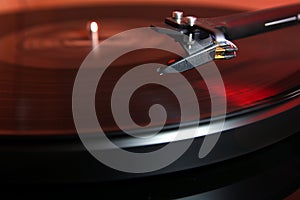 Cartridge of a modern high quality turntable record player about to be lowered onto a vinyl analogue music LP with red backlight.
