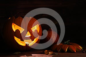 Carved halloween pumpkin with a scary glowing face on dark rustic wood as an autumn decoration, copy space