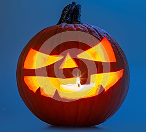 Carved pumpkin for Halloween jack-o'-lanterns with scary smiles and burning candle inside isolated on blue background