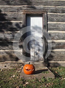 Carved Pumpkin sits on a Door Step of a Log Cabin