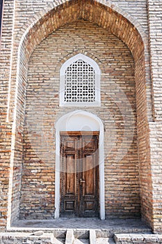 carved wooden door with oriental Uzbek pattern in brick wall with arch in Barak-Khan Madrasah in Tashkent in Uzbekistan