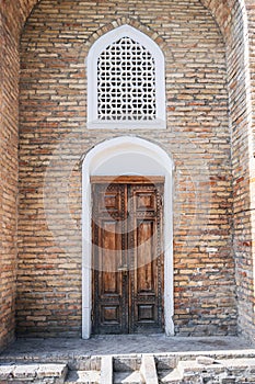 carved wooden door with oriental Uzbek pattern in brick wall in Barak-Khan Madrasah in Tashkent in Uzbekistan