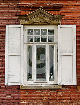 A carved wooden window with shutters on the facade of an old brick building