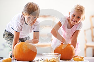 Carving pumpkins is a family tradition. Portrait of a little boy and girl hollowing out their jack-o-lantern.