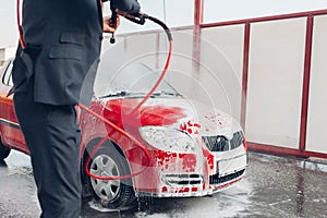 Carwash. Driver covers his auto with soap foam and cleans it with water with high pressure.