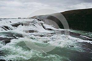 Cascade waterfall in Iceland. White splashes, turquoise water, and black rock under the gray sky. Spring