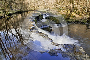 Cascade and waterfall on the River Neath reflecting trees and blue skies