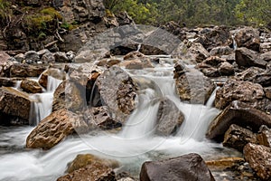 A cascading mountain stream bends and weaves around rocks and boulders, long exposure to create motion blur to the water