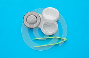 Case with contact lenses and tweezers on light blue background, flat lay