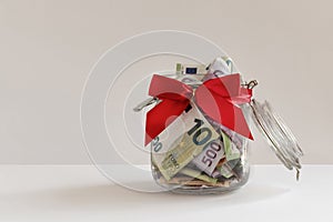 Cash euro banknotes in gift money box. Glass jar piggy bank, money and red bow. Cash reward, gift Background, copy space