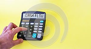 Cash flow on the display of the calculator on a yellow background. Male hand on a calculator