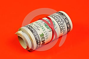 Cash hundred-dollar bills in a roll, tied with a red ribbon, on a red background.