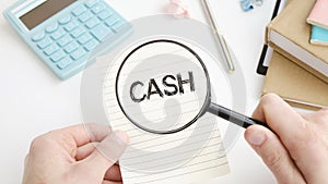 CASH text on paper sheet with magnifying glass