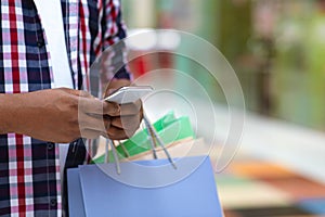 Cashback Concept. Man With Shopper Bags Using Smartphone In Mall During Shopping