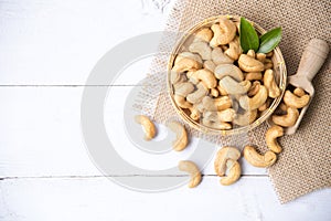 Cashew nuts with green leaves in basket and spoon isolated on white wooden background