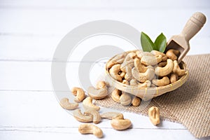 Cashew nuts with green leaves in basket and spoon isolated on white wooden background