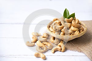 Cashew nuts with green leaves in basket and spoon isolated on white wooden background