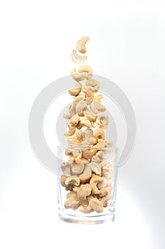 Cashew nuts spill out of a glass on a white background