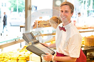 Cashier in baker's shop posing with cash register