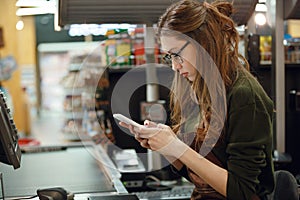 Cashier lady on workspace in supermarket shop using mobile
