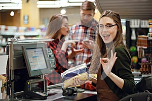 Cashier woman on workspace make okay gesture.