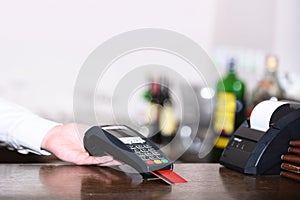 Cashiers hand holds credit card reader on light defocused background.