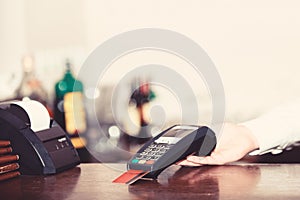 Cashiers hand holds credit card reader on light defocused background.