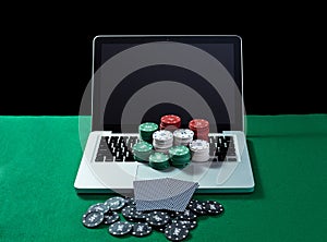 Casino chips and cards on keyboard notebook at green table.