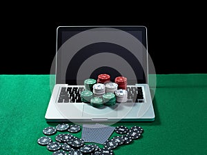 Casino chips and cards on keyboard notebook at green table.