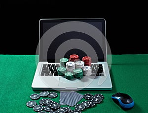 Casino chips and cards on keyboard notebook at green table.