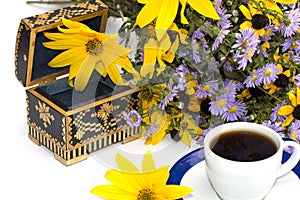 Casket, cup of coffee, bouquet of wild flowers and yellow flower