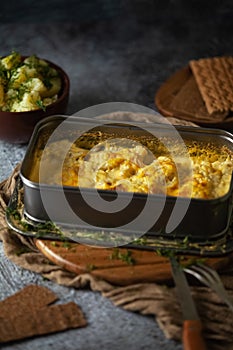 A casserole with baked fish and cheeze sauce on the dark background, potatoes in a clay bowl