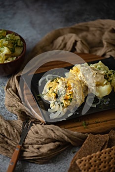 A casserole with baked fish and cheeze sauce on the dark background, potatoes in a clay bowl