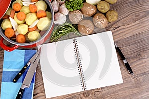 Casserole dish with vegetables and cookbook on kitchen table, copy space