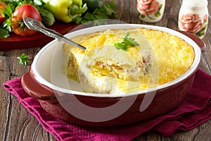 Casserole with potatoes, meat and cheese on a wooden table.