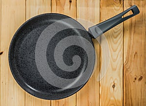 Cast-iron frying pan with non-stick coating against a background of a woody texture