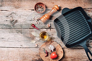 Cast iron pan, spices, pepper shaker, meat fork, oil, spices on wooden background. Top view. Copy space. Healthy, clean food and