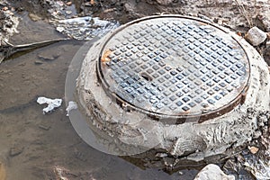 A cast-iron sewer manhole surrounded by a puddle of water at a construction site. Construction of sewer wells