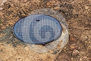 A cast-iron sewer manhole surrounded by a puddle of water at a construction site. Construction of sewer wells