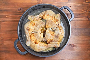 Cast iron skillet with fried chicken legs with spices on a wooden table
