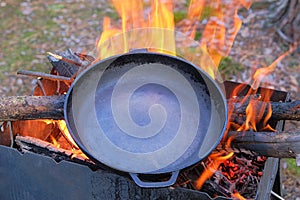 Cast iron skillet over an red fire heats up for further cooking. Firing a cast iron skillet over an open fire