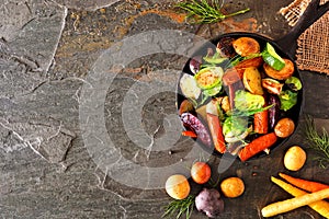 Cast iron skillet of roasted autumn vegetables, above view side border on a dark slate background