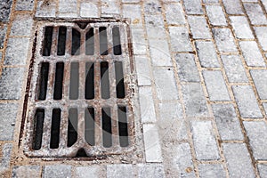 A cast-iron storm sewer hatch on the road lined with paving slabs. Drainage of rainwater from the surface of the sidewalk. Close-