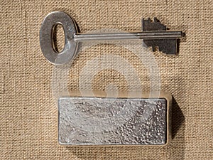Cast silver bars and the key to the safe against a rough texture of the fabric