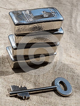 Cast silver bars and the key to the safe against a rough texture of the fabric
