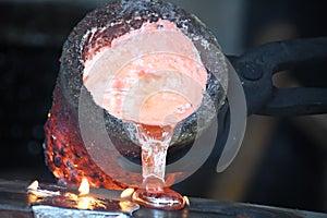Casting liquid red hot metal from crucible held with tongs