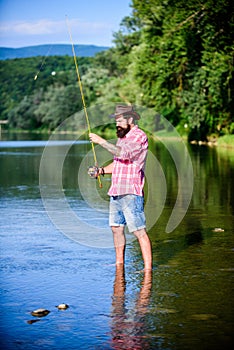 Casting off. mature bearded man with fish on rod. successful fisherman in lake water. hipster fishing with spoon-bait