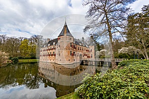 Castle of Het Oude Loo with its bridge reflected in the water surface of its moat among trees and green vegetation