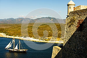 Castle San Pedro de la Roca del Morro, in Santiago de Cuba. Sailing boat leaving the harbor in the background