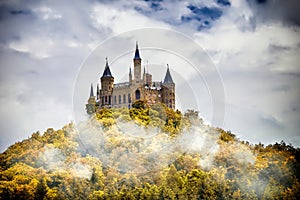 Castle on a wooded mountain in the fog under clouds